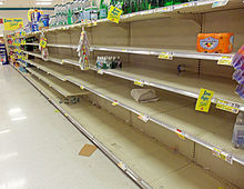 A supermarket aisle with a large section empy save for scattered packages of bottled water